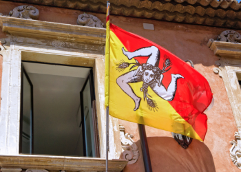 The Trinacria symbol of Sicily on a flag outside a window in Sicily.