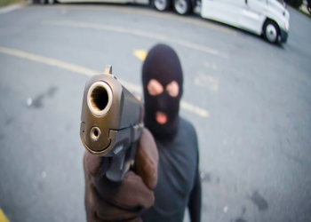 A photo of a masked man pointing a gun at the cab of a truck.