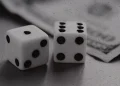 A black and white photo of a pair of dice next to a stack of hundred dollar bills.